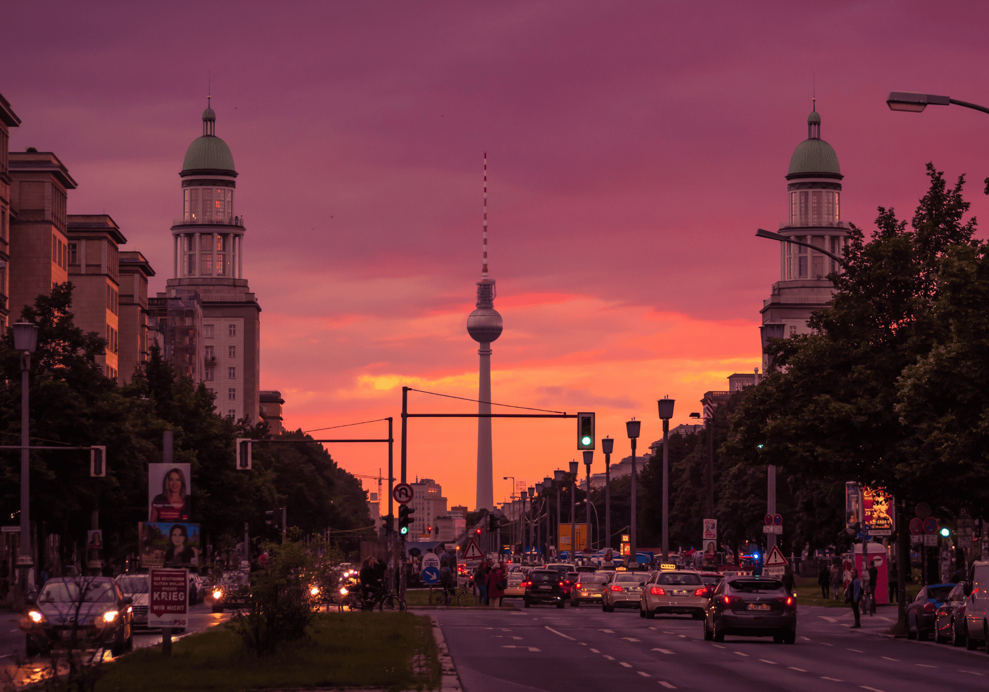bild vom berliner fernsehturm bei sonnenuntergang. auf einer breiten straße fahren viele autos. der himmel ist in beere und orange getaucht wie das logo der info gmbh markt und meinungsforschung gmbh