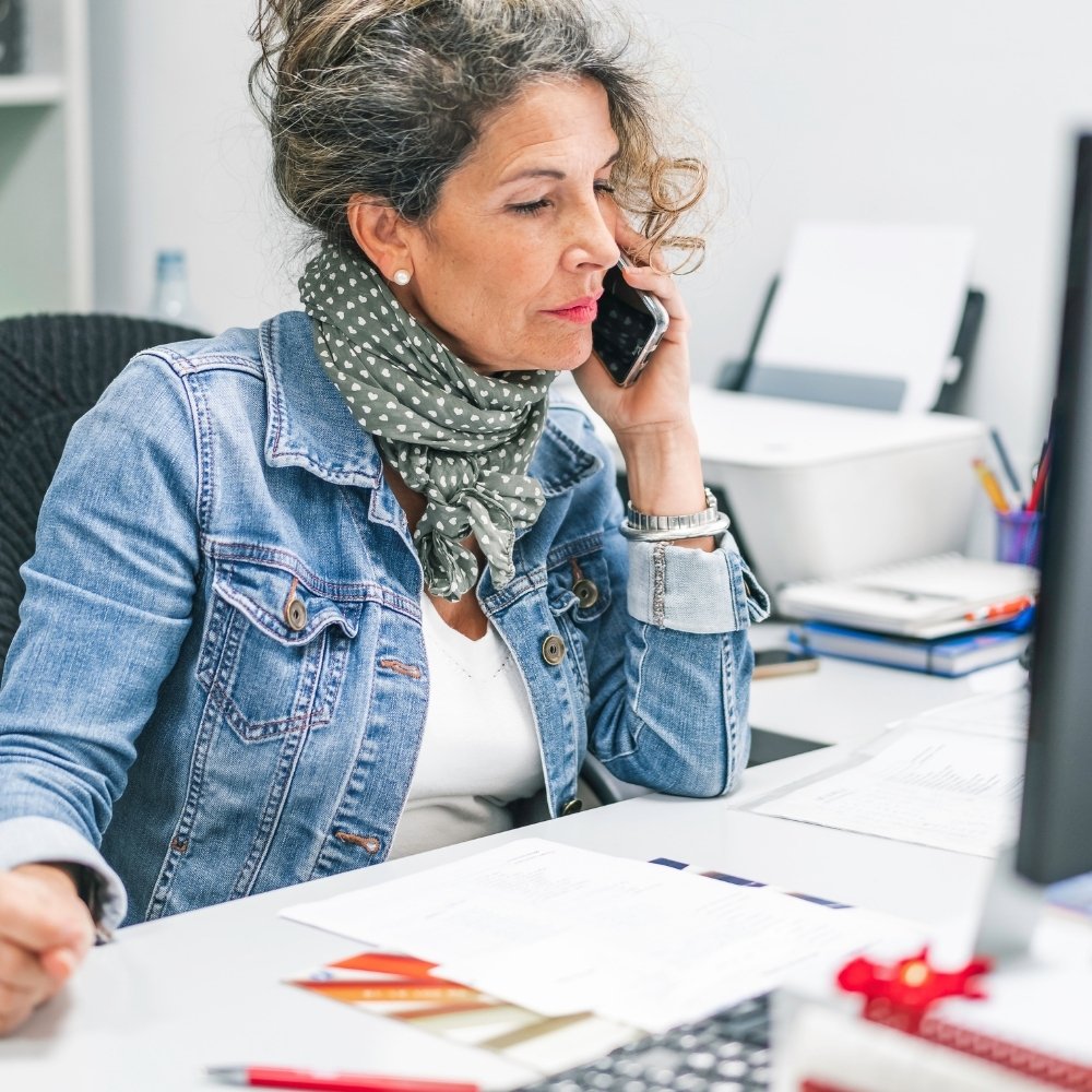 mitarbeiterin der info gmbh sitzt am schreibtisch über einer auswertung einer befragung und telefoniert mit ihrem handy mit dem auftraggeber