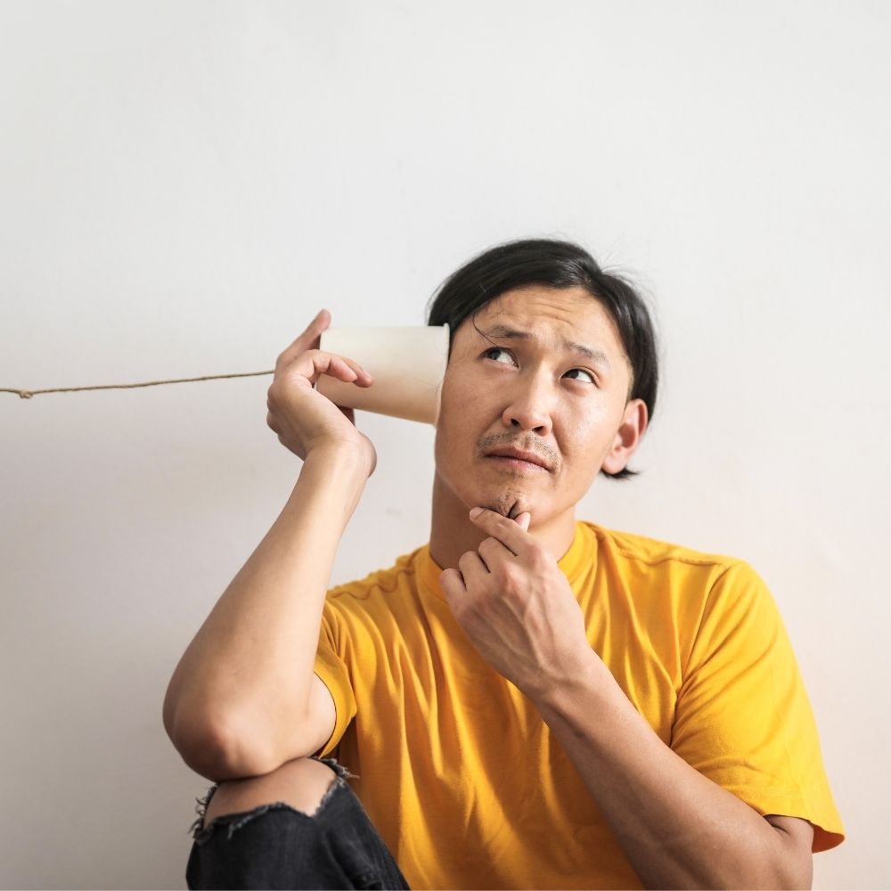 eine person in einem gelben tshirt hält ein selbst gebasteltes telefon mit schnur ans ohr zur seite wir liefern antworten von der info gmbh